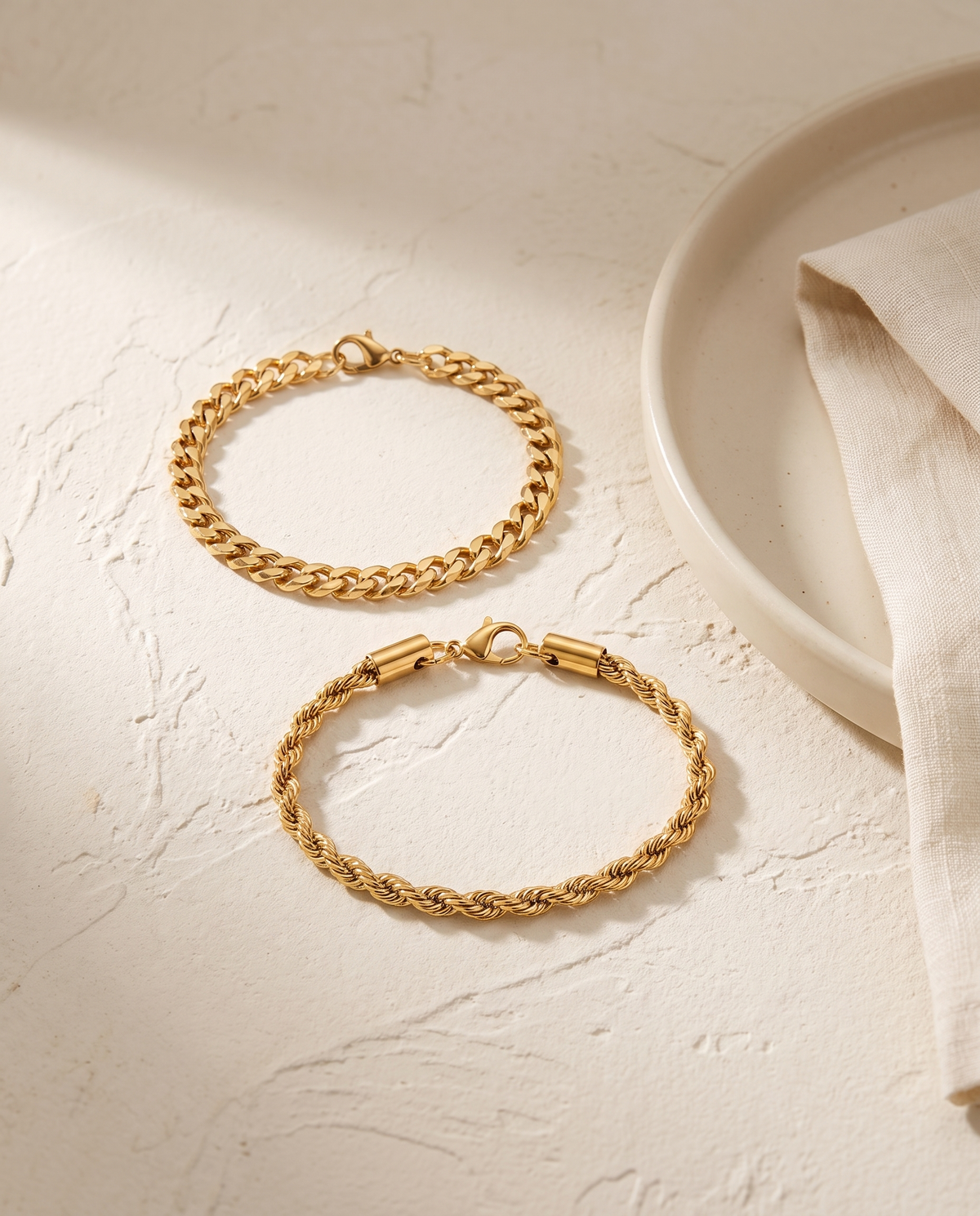 Sablon Stack in gold, both bracelets on warm plaster beside a ceramic dish